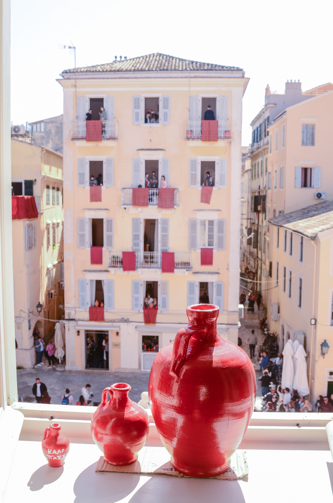 3 red clay pots of different sizes in front of an open window. Opposite, a building with red banners. Botides at a Banknote Museum window
