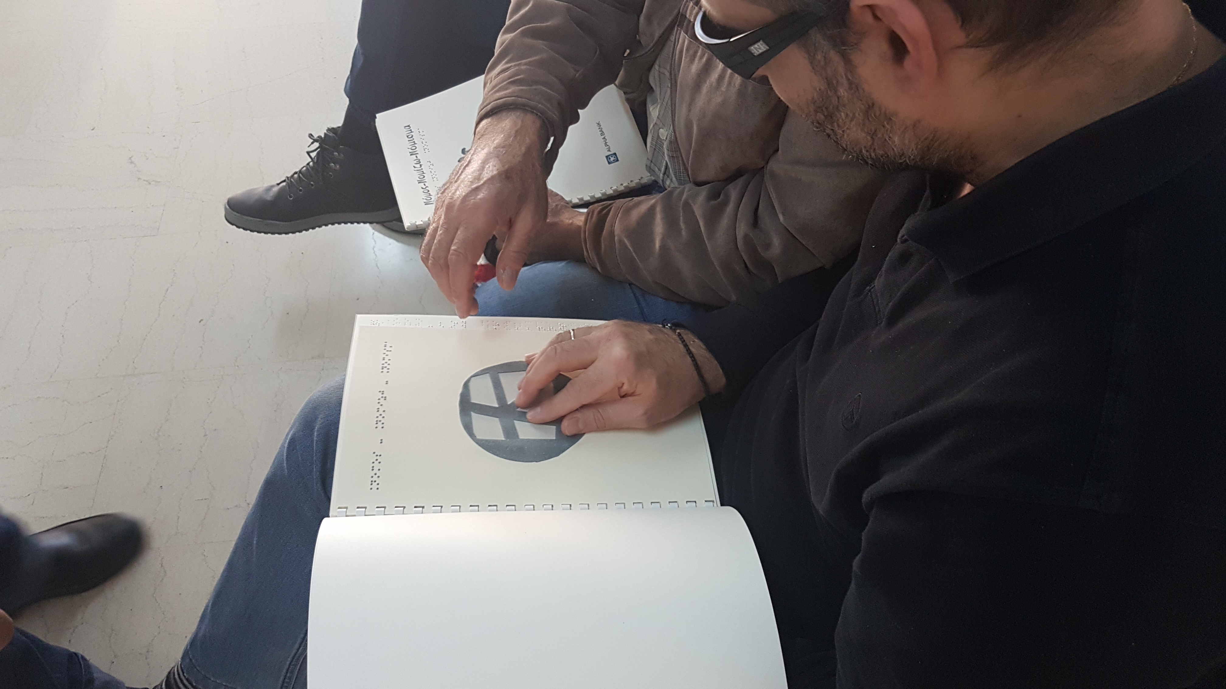 Photograph of a visually impaired person holding a copy of the publication in Braille. Photograph from the event on the history of coins at the Lighthouse for the Blind