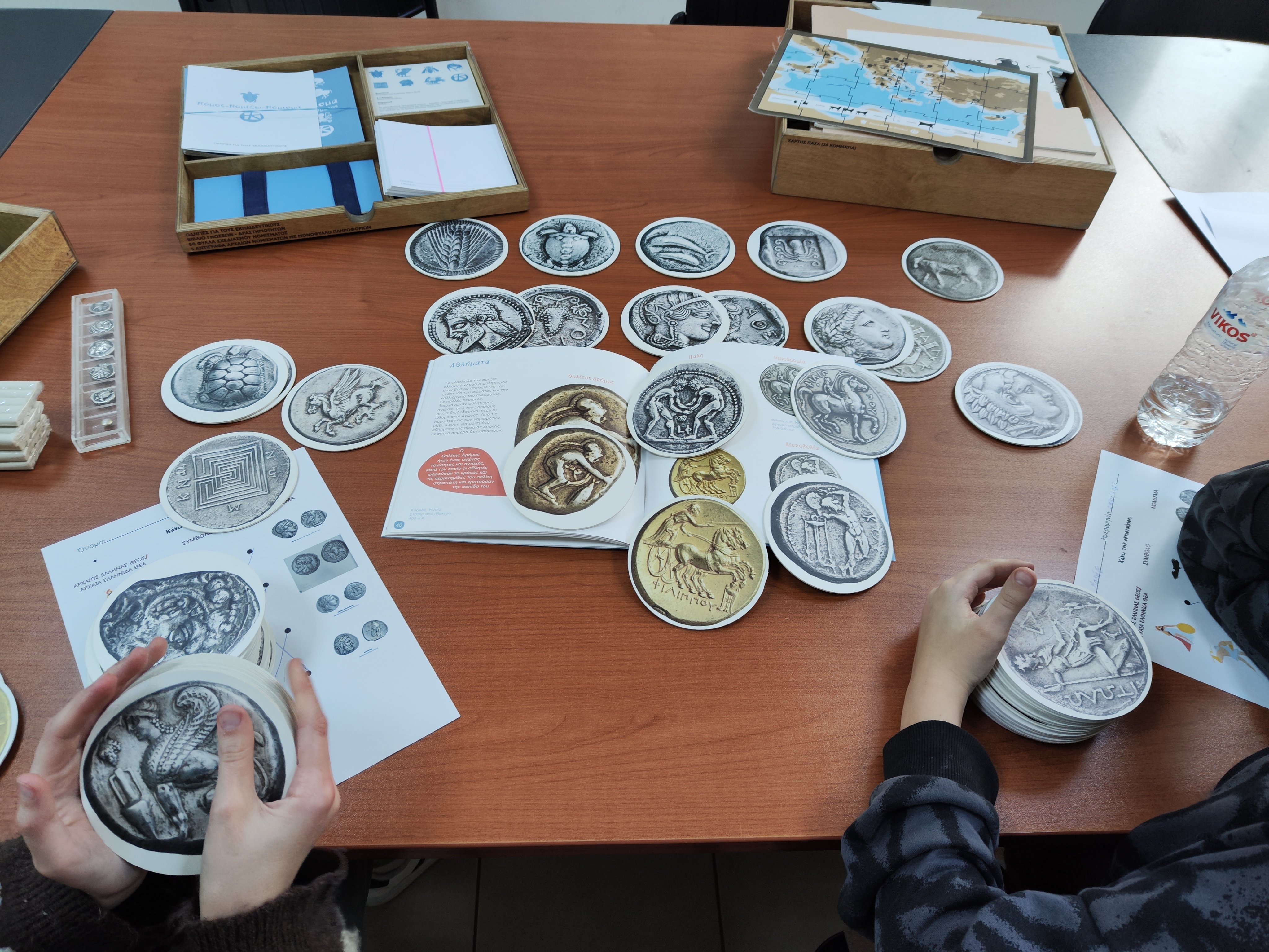2 wooden cases with educational material and paper coin replicas spread on a table. Snapshot from educational programme