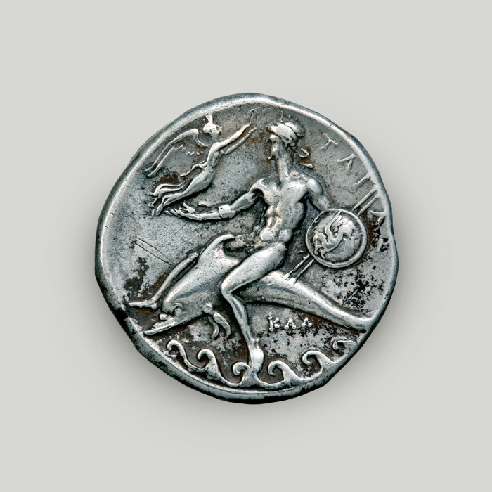 Reverse of Tarentum silver stater depicting a hero astride a dolphin swimming on the waves.   Reverse of Tarentum silver stater