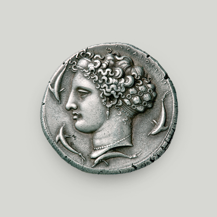 Οπίσθια όψη με κεφαλή της Αρέθουσας με 4 δελφίνια γύρω που κολυμπούν και χαραγμένη τη λέξη ΣΥΡΑΚΟΣΙΩΝ.  Οπίσθια όψη αργυρού δεκάδραχμου Συρακουσών, Σικελία