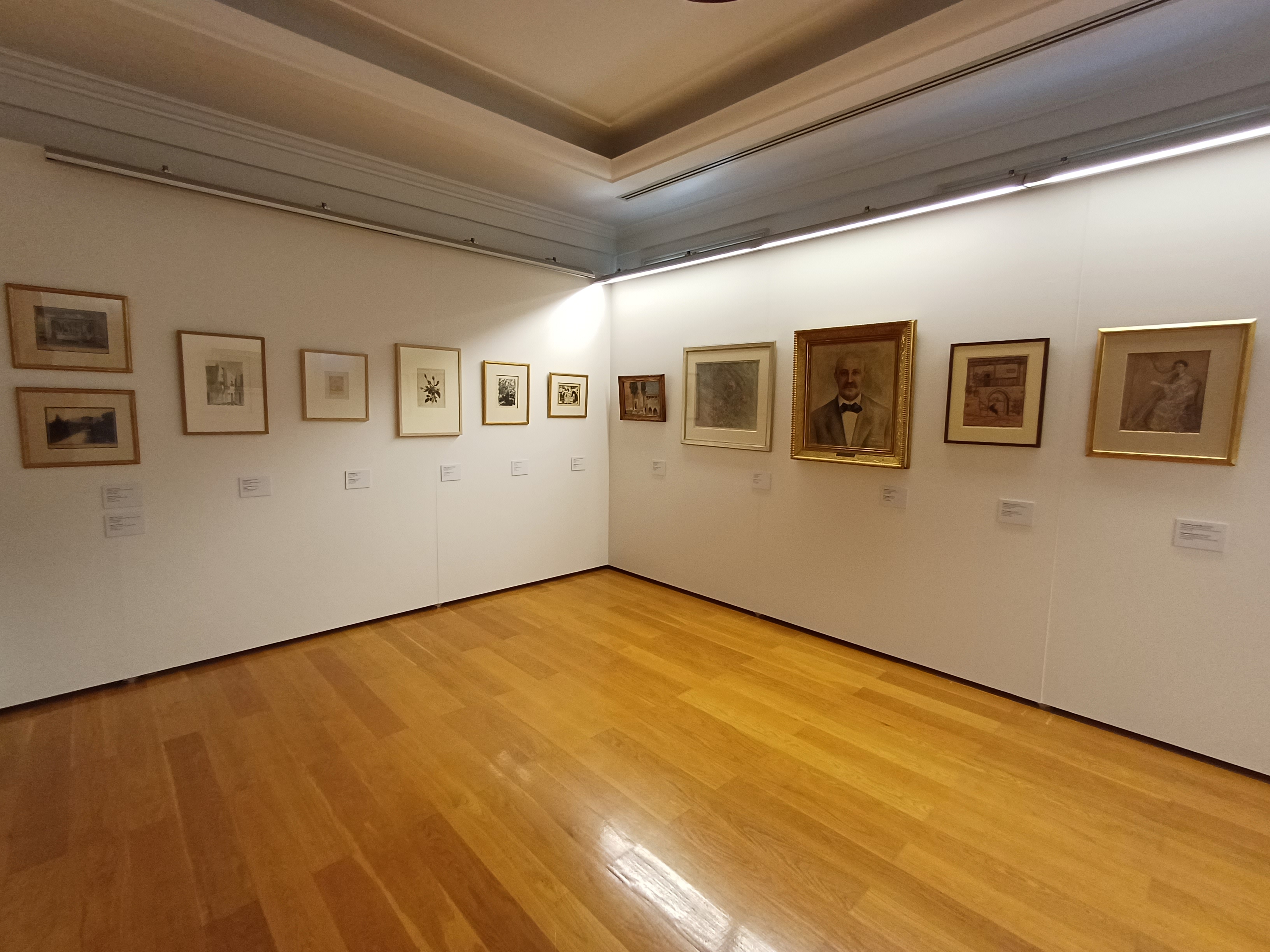 Πίνακες σε λευκούς τοίχους. Αριστερά, ασπρόμαυρες φωτογραφίες. Δεξιά, 2 πορτρέτα και 3 μικρότεροι πίνακες. Φωτογραφία από τους χώρους της έκθεσης