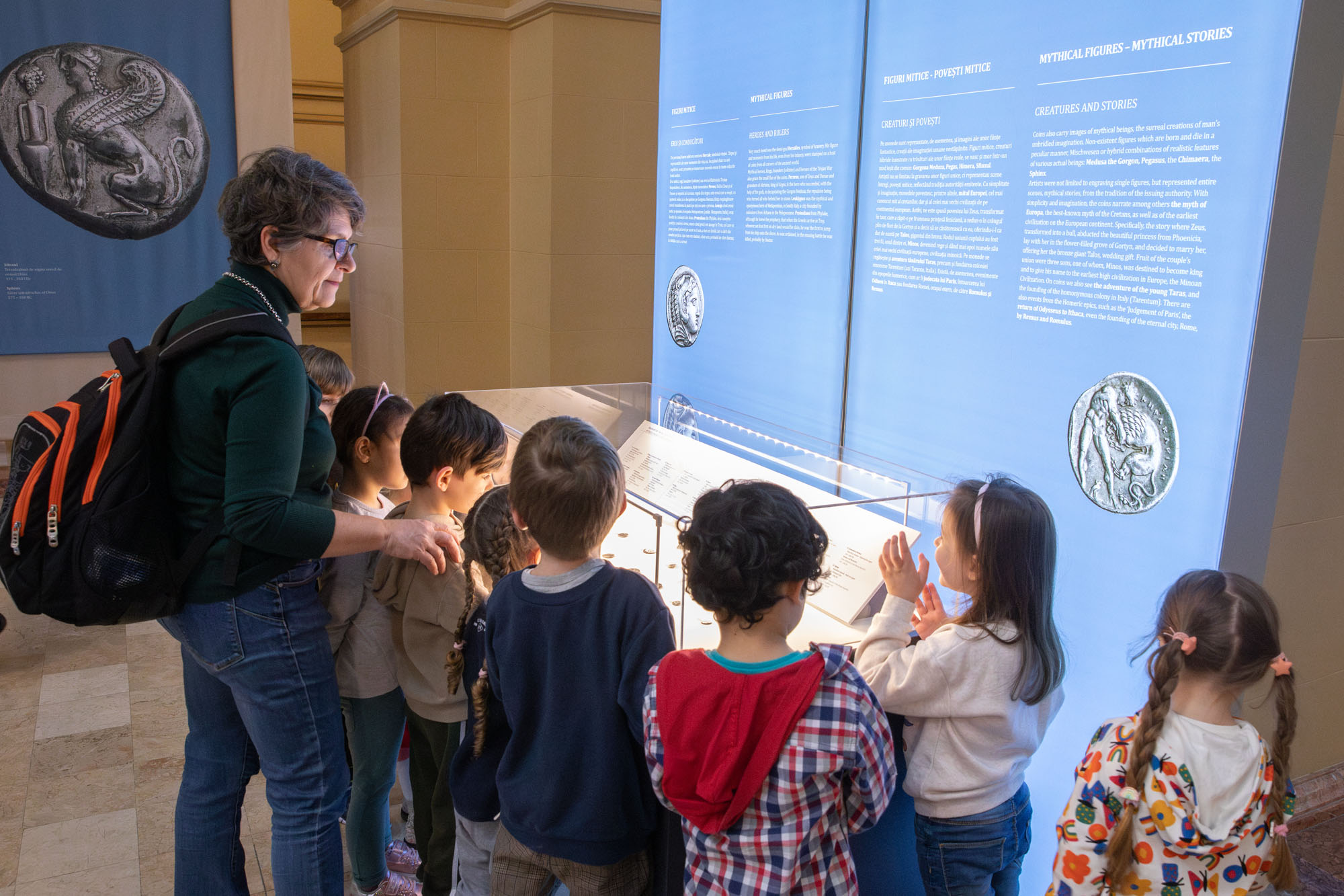 A teacher and school children observing coins in a glass display case. Highlight from the guided tour