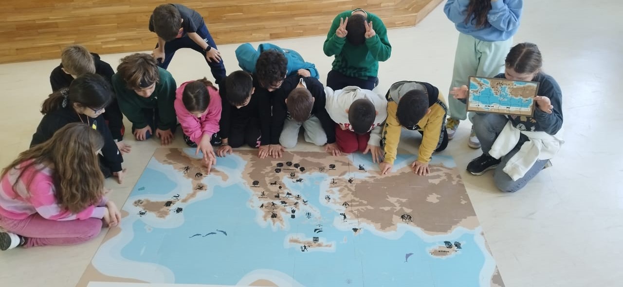 Children sitting on the floor and looking at the programme’s floor map-puzzle. Snapshot from educational programme