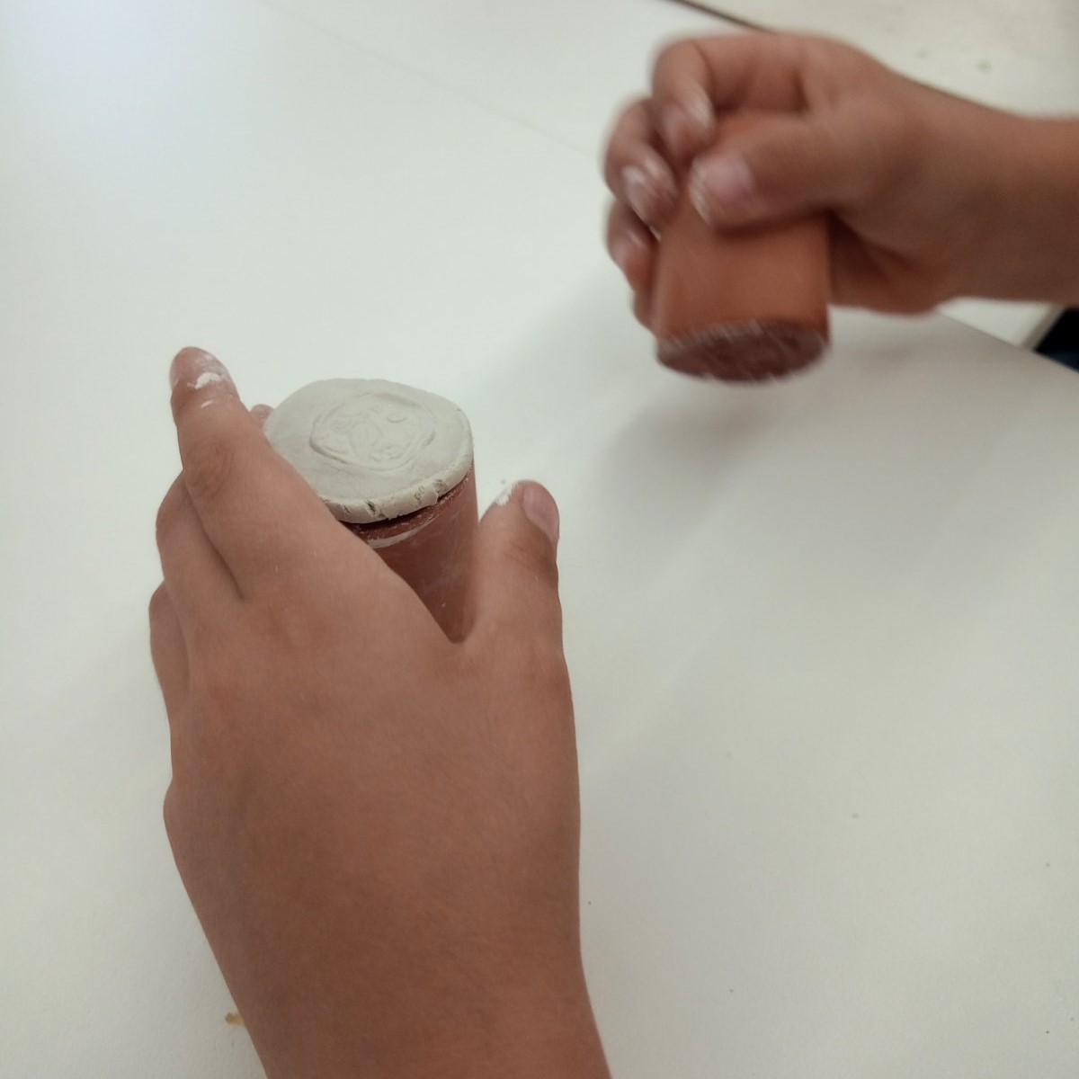 Children's hands make coins with plasticine using clay moulds on a white table. Highlight from the programme