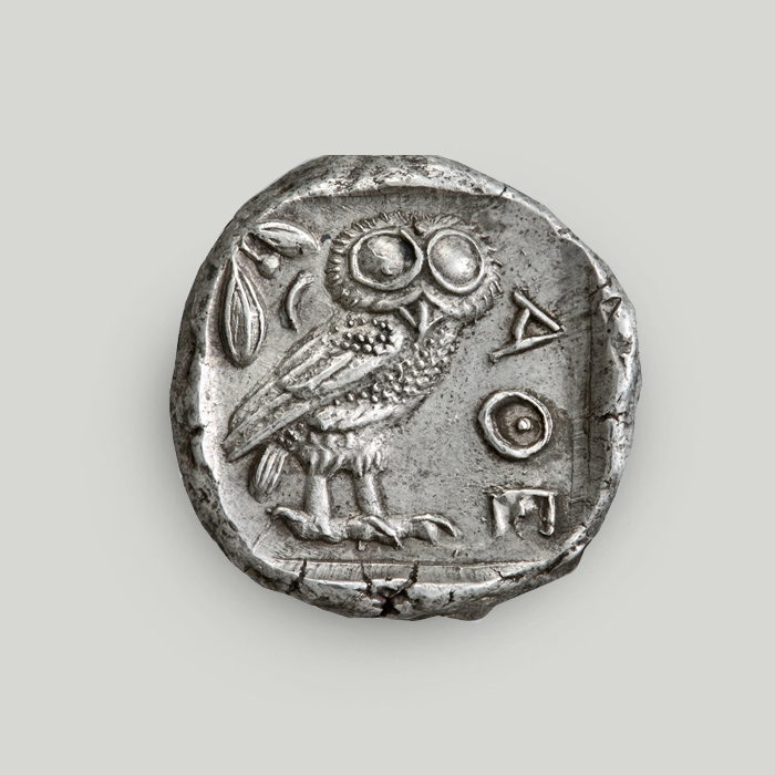 Οπίσθια όψη αργυρού τετράδραχμου Αθήνας με την κουκουβάγια και κάθετα χαραγμένη την επιγραφή ΑΘΕ.  Οπίσθια όψη αργυρού τετράδραχμου Αθήνας