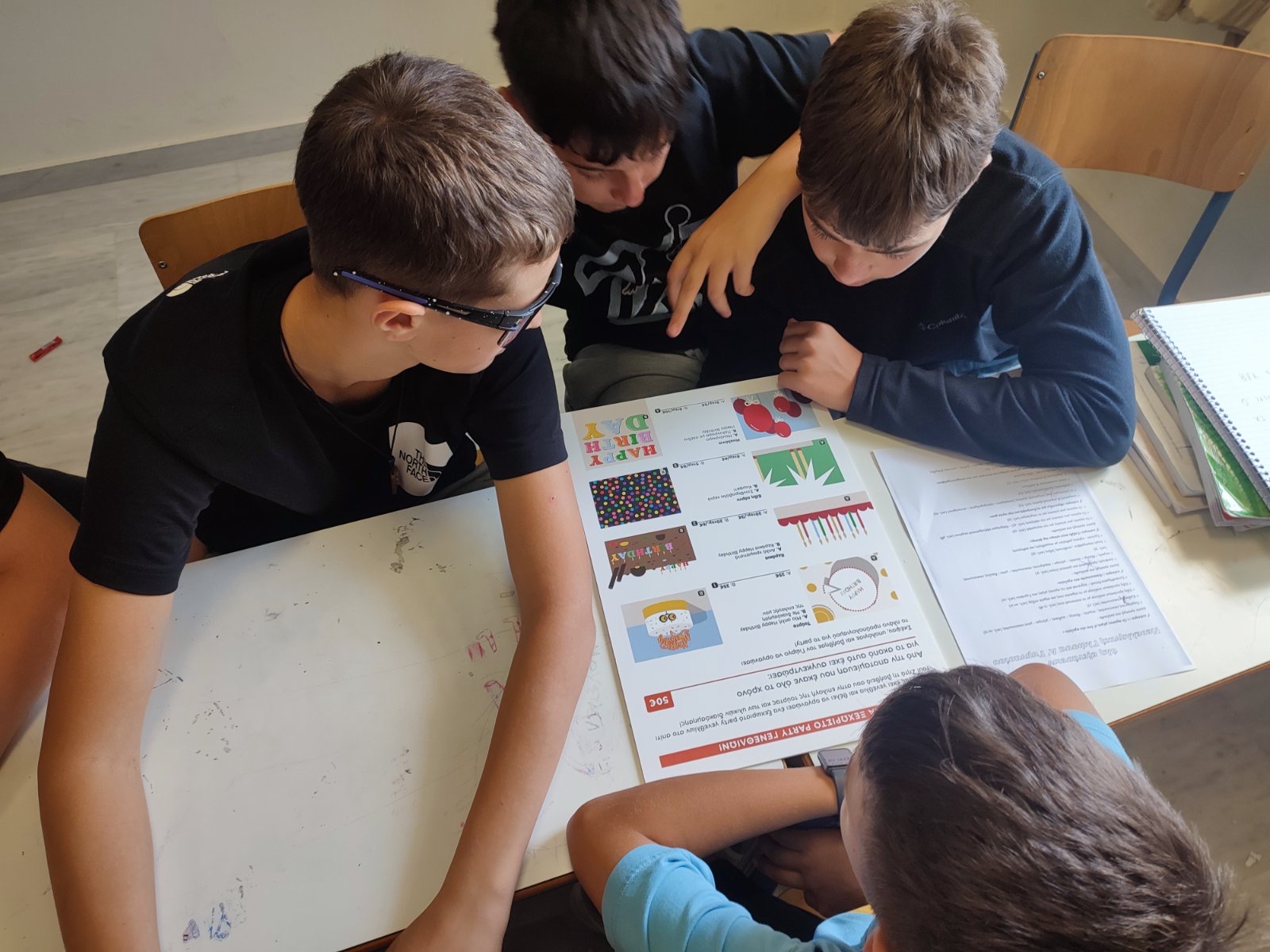 4 boys gathered around programme material, working on an activity.   Snapshot from educational programme