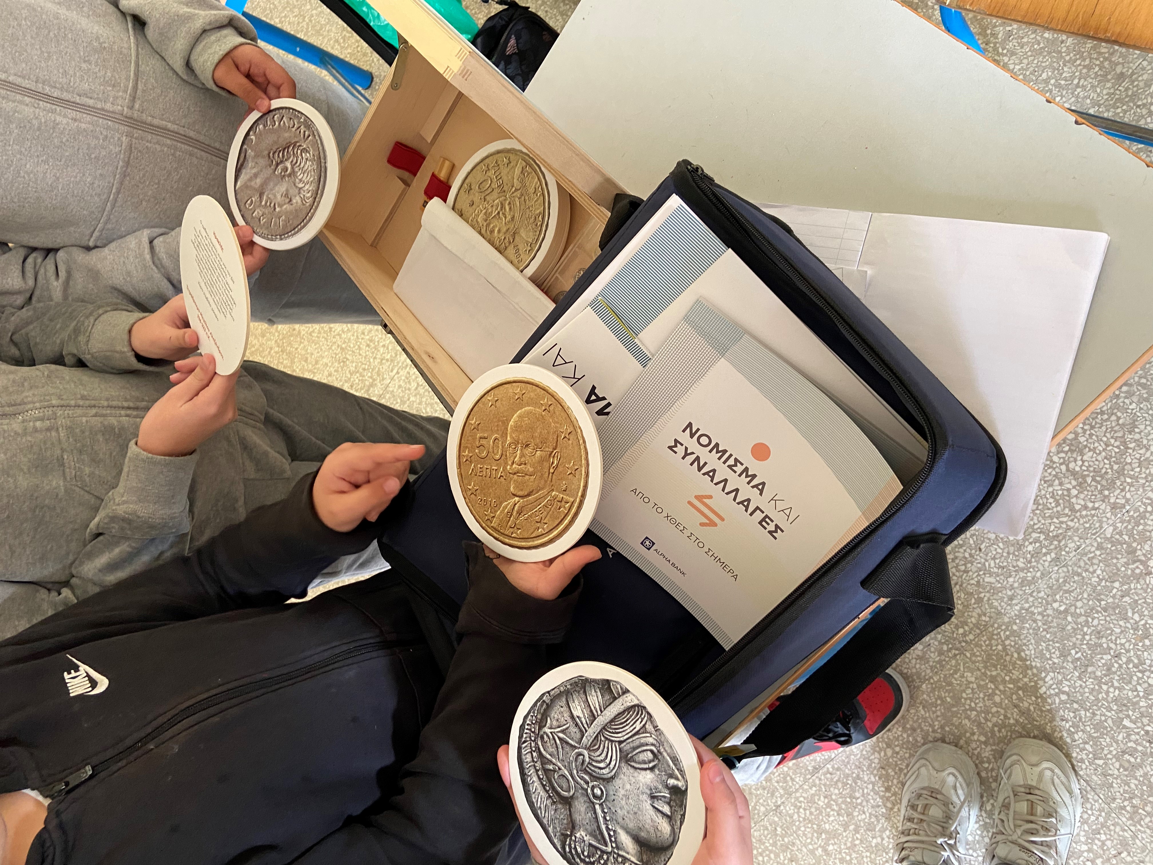 Students in front of an open museum kit with coin replicas and brochures.  The Currency and Transactions museum kit at a Cyprus school