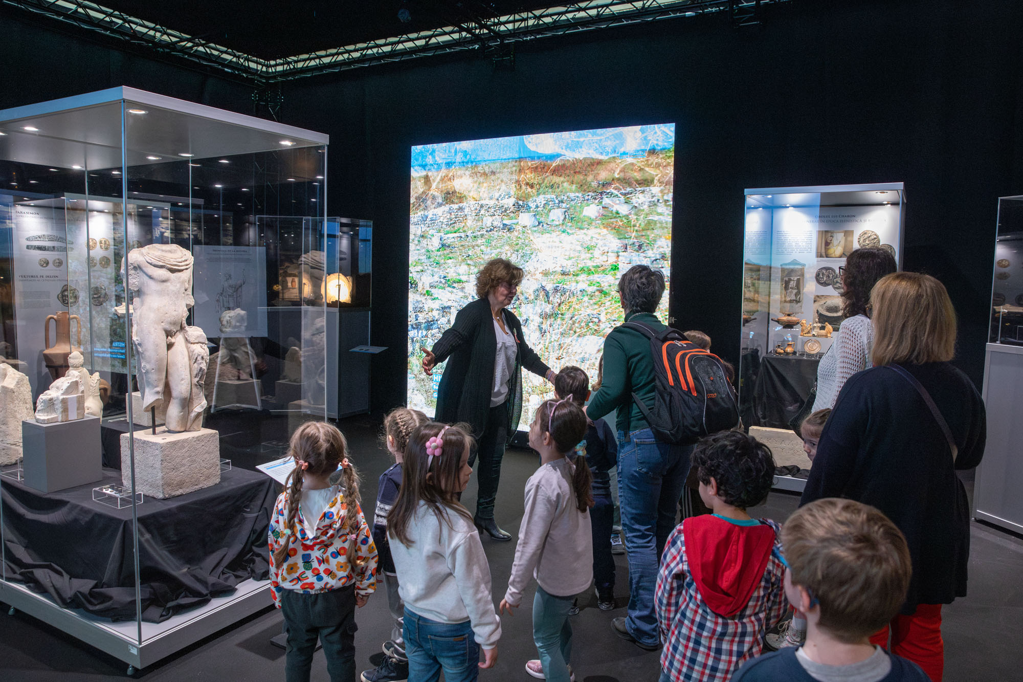 Ms Tsangari talking to students and teachers in front of a glass display case next to a marble male figure and other sculptures. Highlight from the guided tour