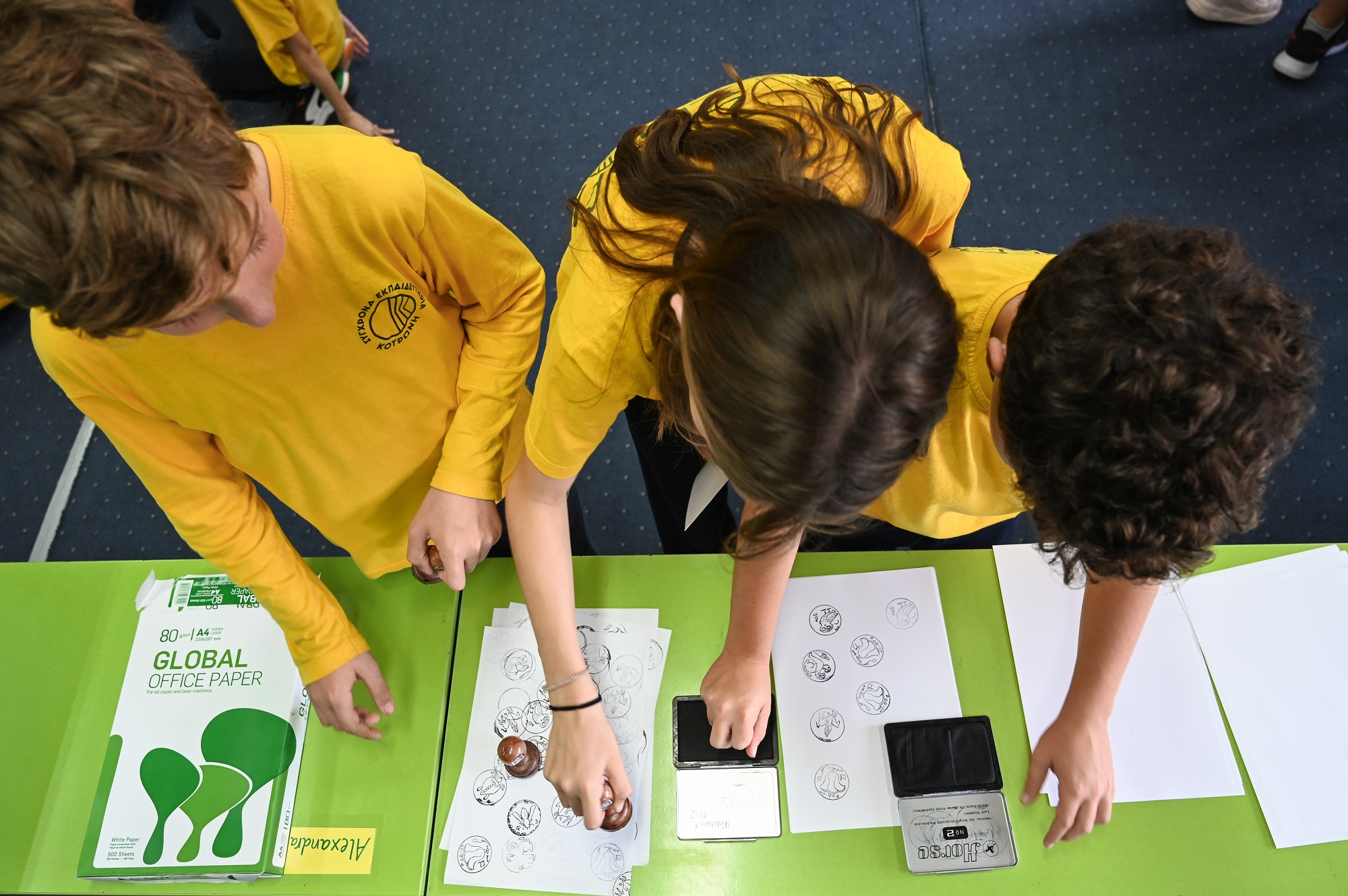 Two boys and one girl placing coin stamps on white sheets of paper. Highlight from the activity
