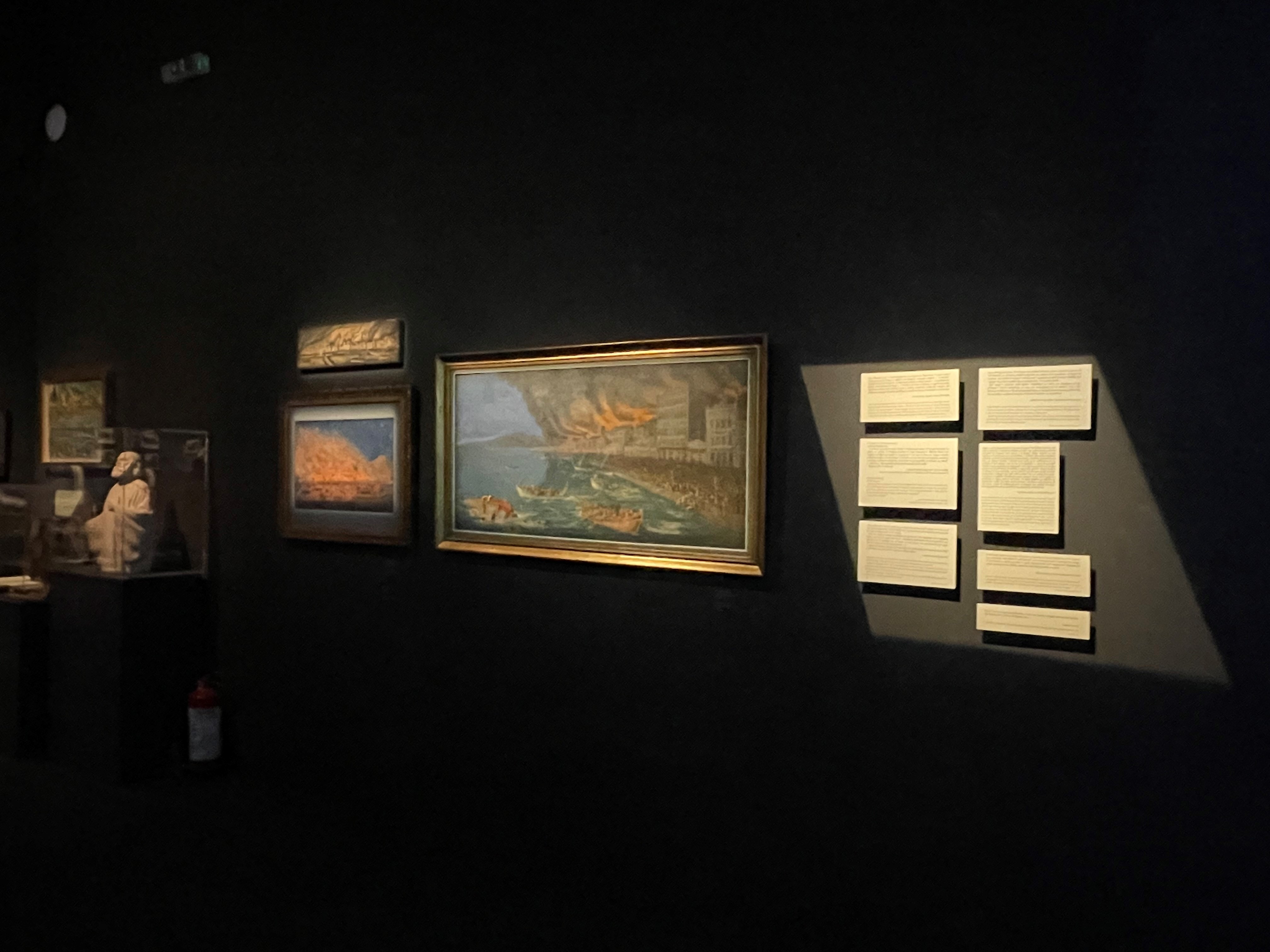 Paintings on a black wall depicting scenes from the Smyrna Catastrophe.  Participation “Asia Minor: Splendour – Catastrophe – Uprooting – Regeneration”