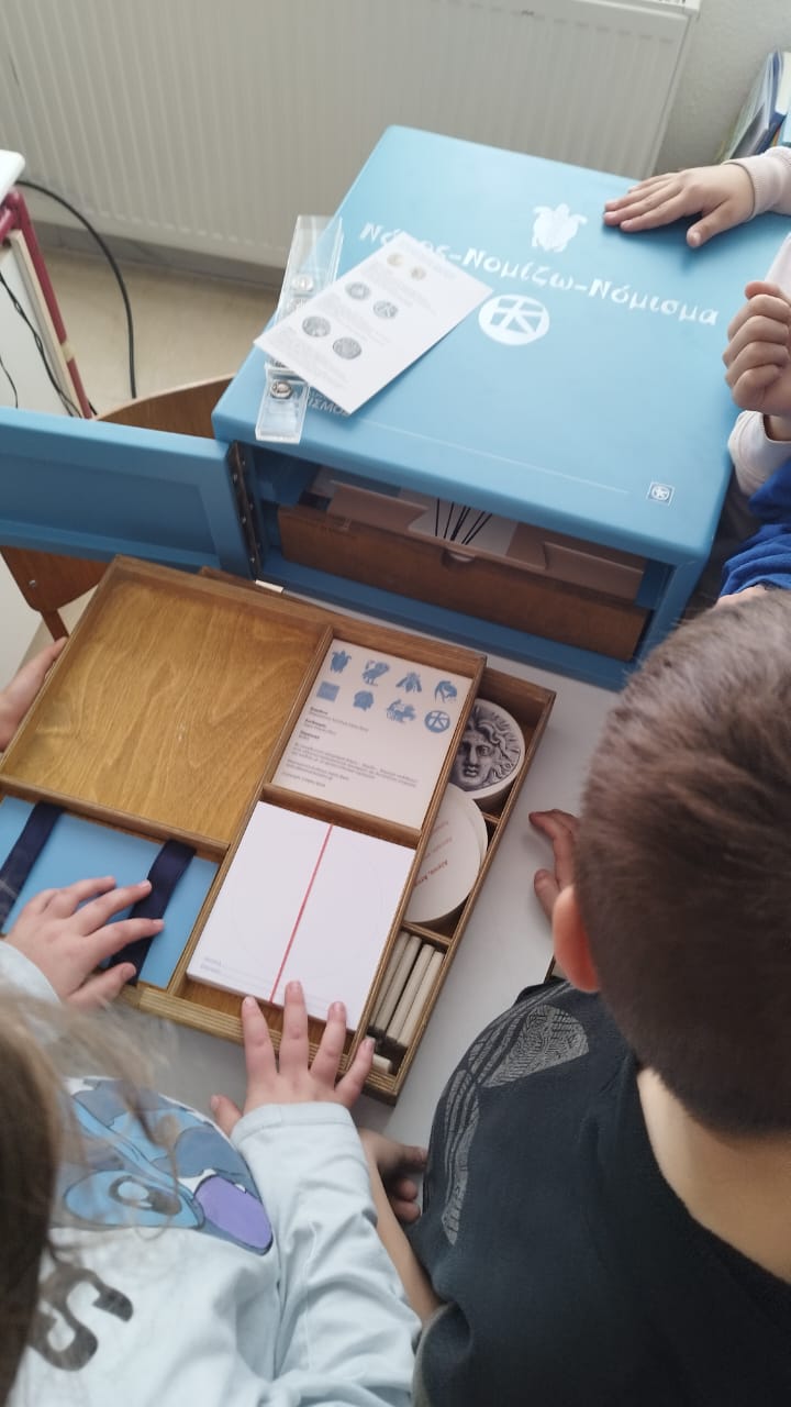 Children looking at the content of the “Nomos-Nomizo-Nomisma” museum kit. Snapshot from educational programme