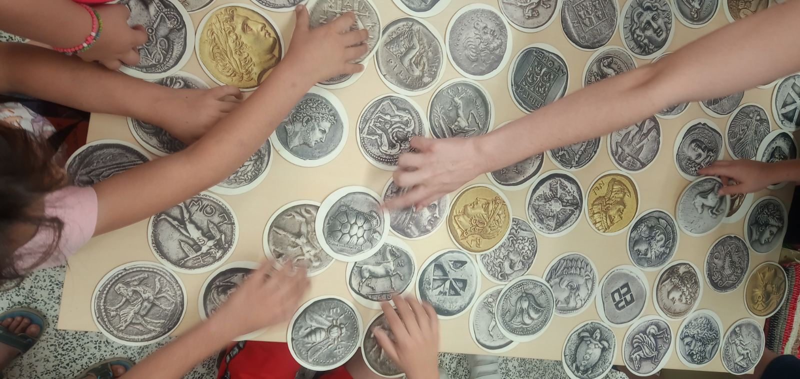 Children’s hands examining coin cards that are spread on a table. Highlight from the programme