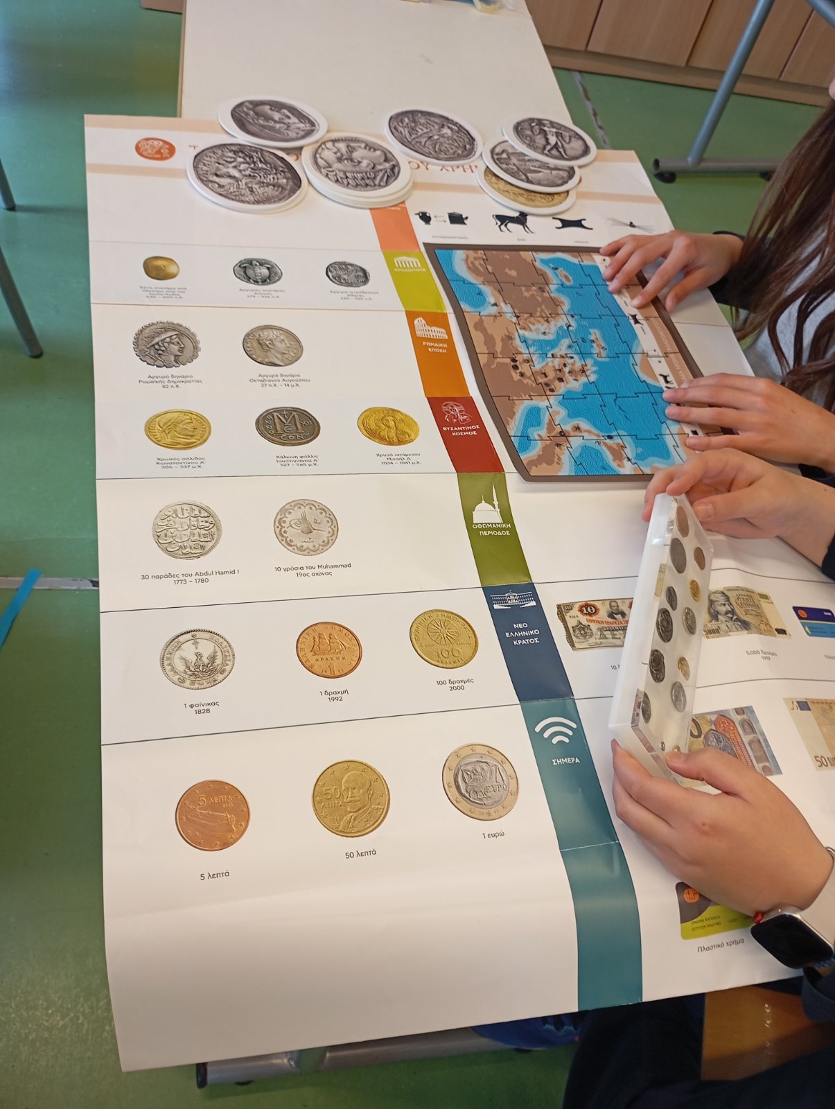 Children examining a brochure with coins of different eras, and a map. Next to them, coin cards. Snapshot from educational programme