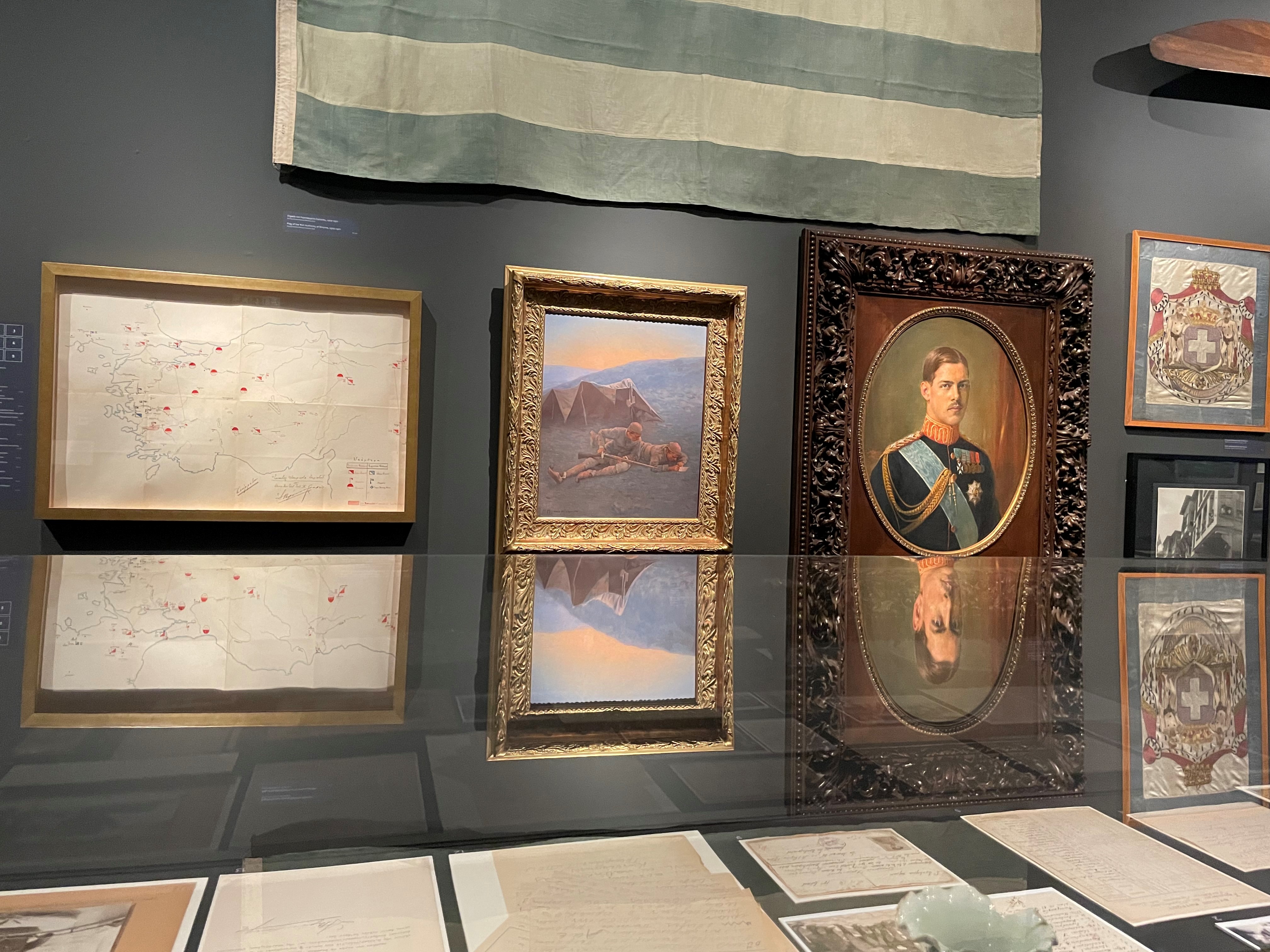 Map, paintings and coat of arms on wall. The Portrait of King Constantine is also visible.  Participation “Asia Minor: Splendour – Catastrophe – Uprooting – Regeneration”