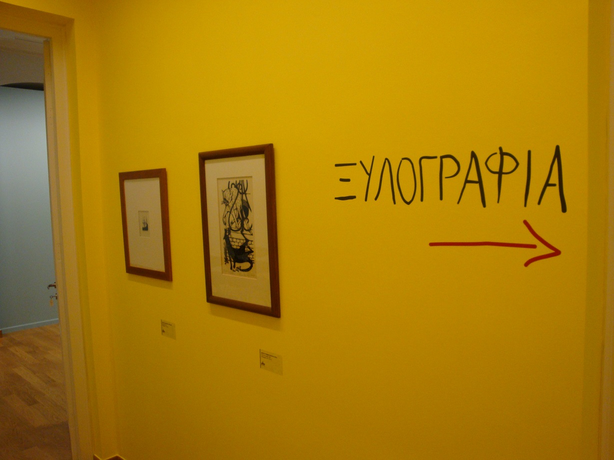 Corridor in the exhibition venue with the word “WOODCUT” on the wall and a pointer arrow.  Directions to the exhibition “Printmaking and its techniques”