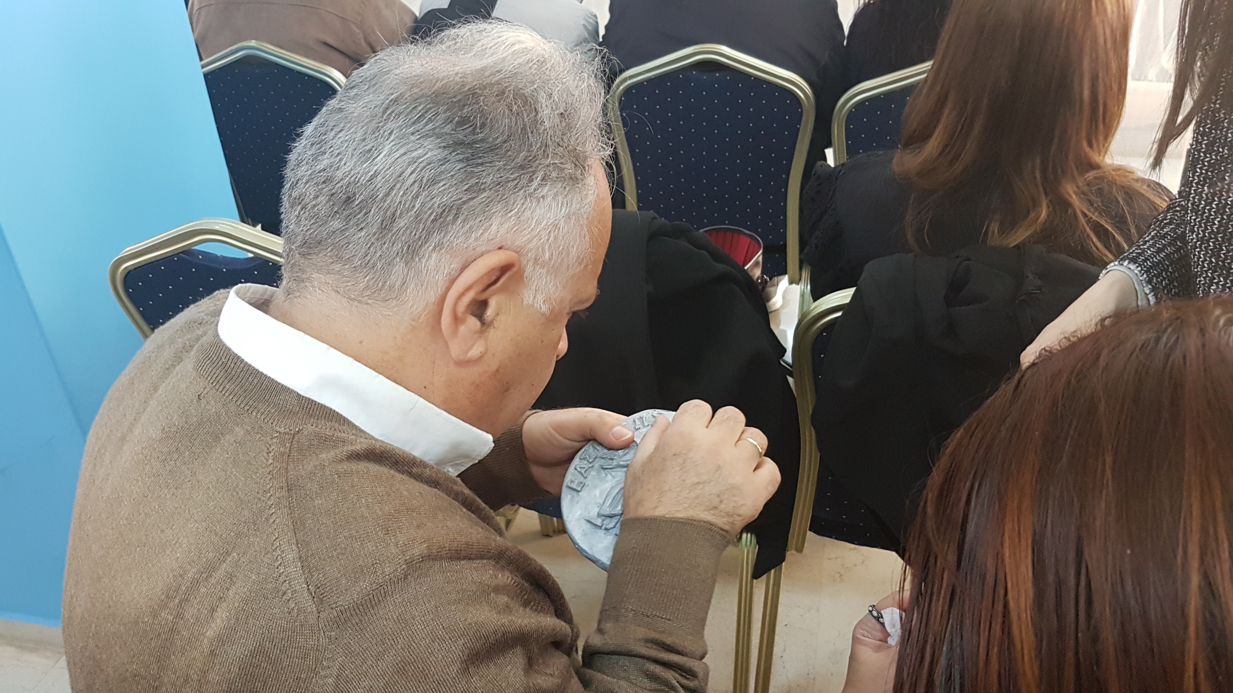 Photograph of a visually impaired person holding an enlarged coin replica. Photograph from the event on the history of coins at the Lighthouse for the Blind