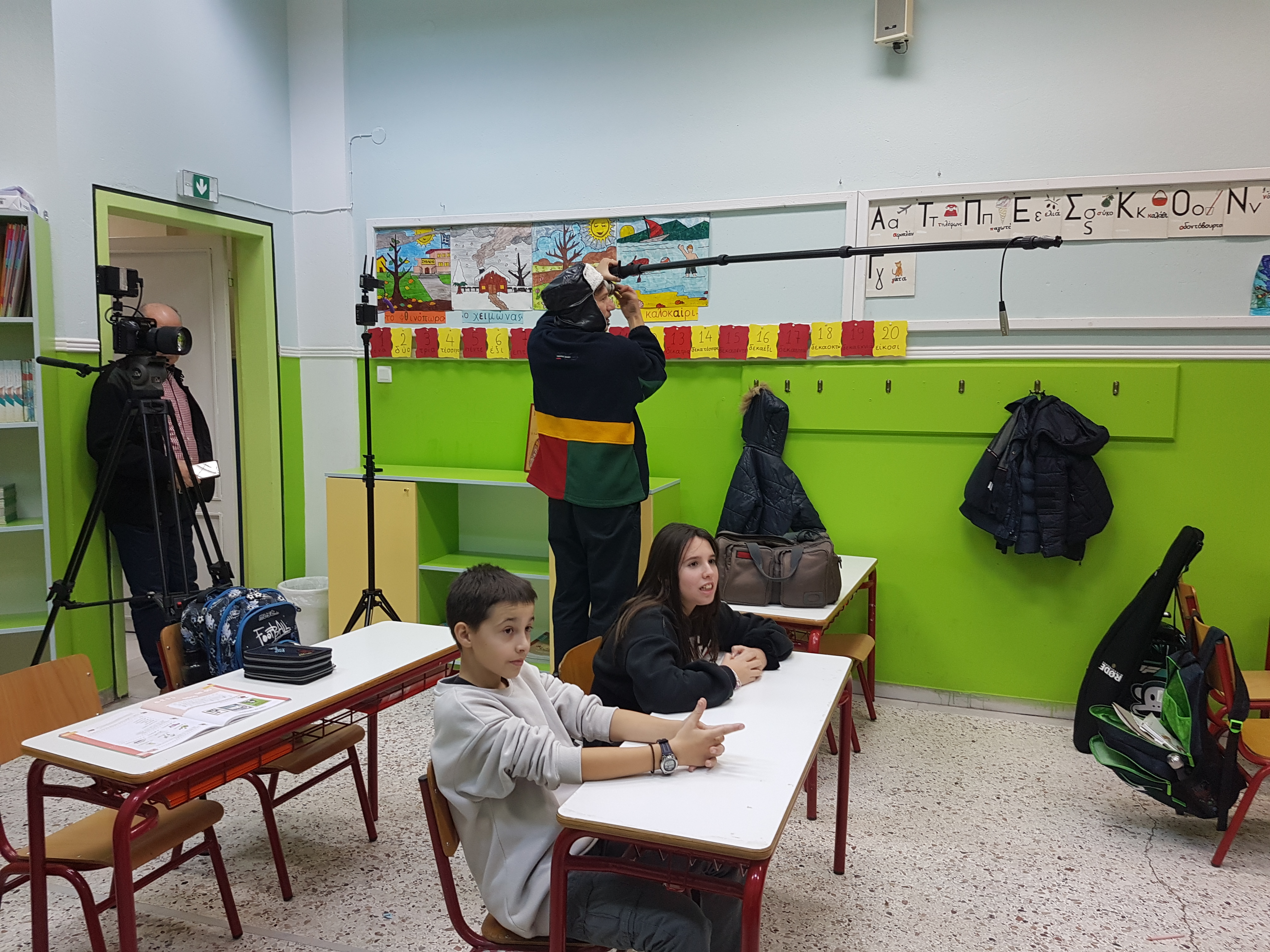 Sound recorder and cameraman standing behind 2 students in a school class.  “Currency and Transactions” museum kit, Kouloura Primary School