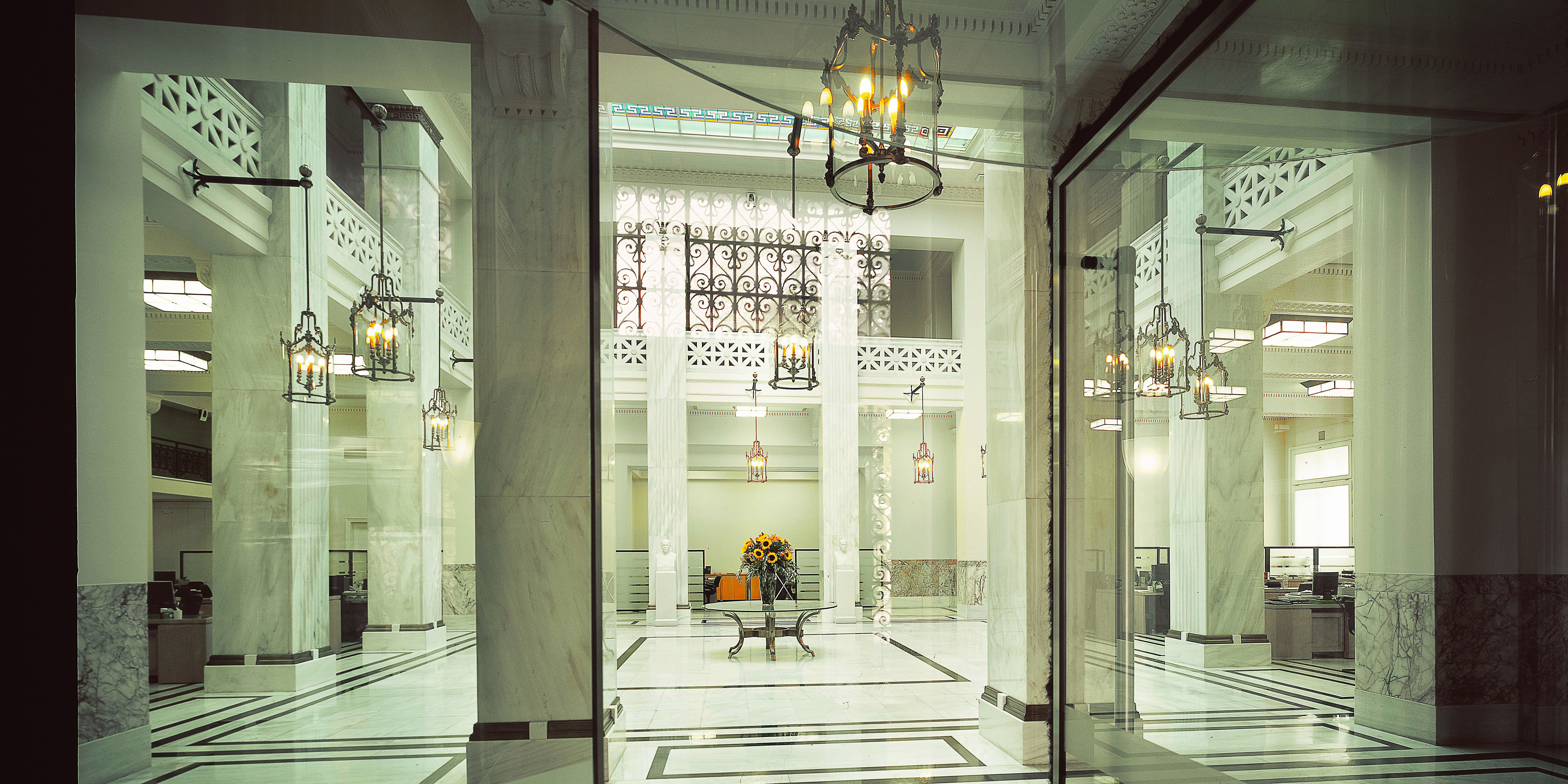 The refurbished main hall of the Popular Bank building, with beige marble surfaces and columns all around.  View of the headquarters’ main hall