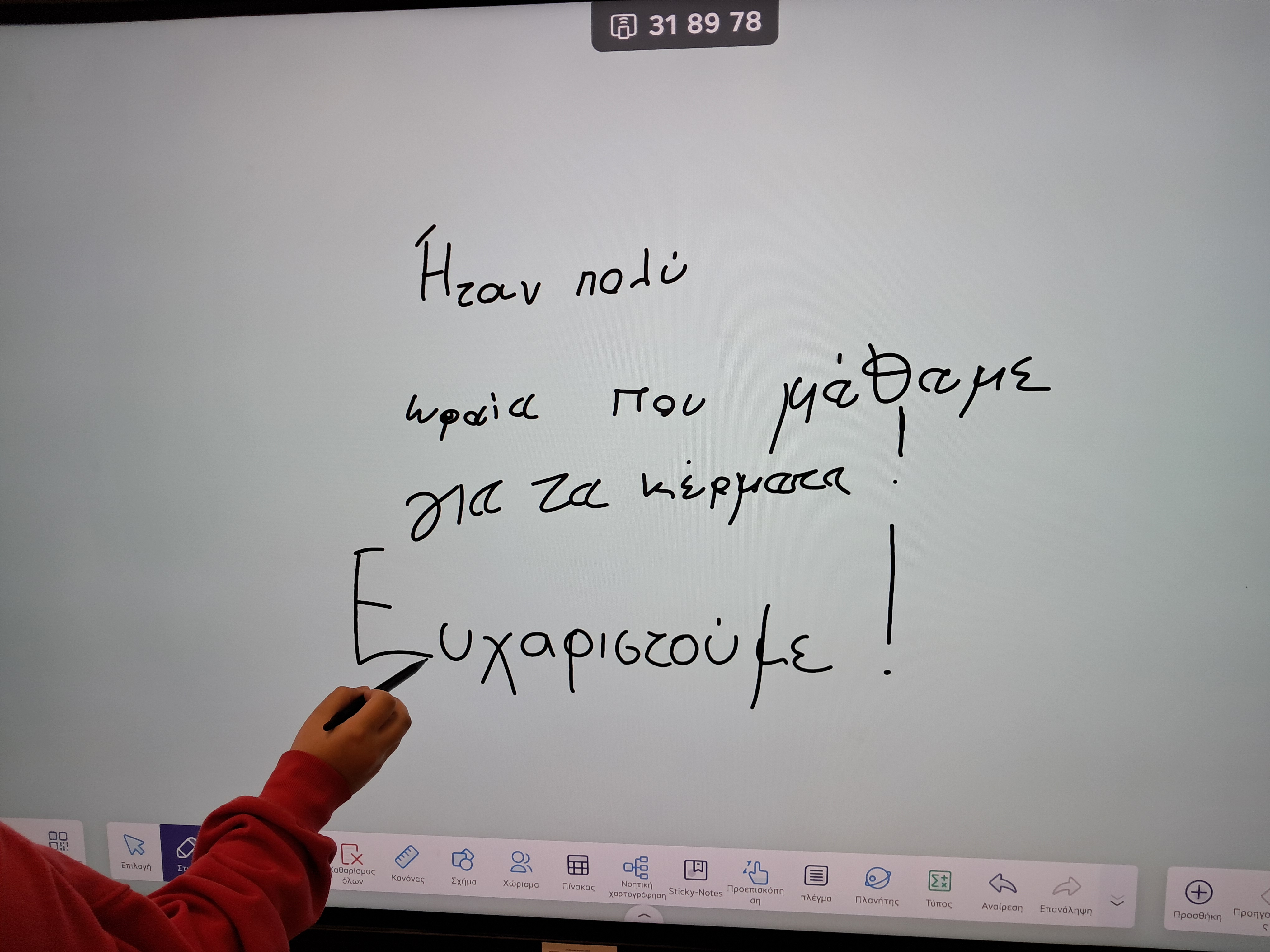 Παιδικό μπροστά από πίνακα. Έχει γράψει: «Ήταν πολύ ωραία που μάθαμε για τα κέρματα! Ευχαριστούμε!» Διαδραστικός πίνακας με παιδικά γράμματα